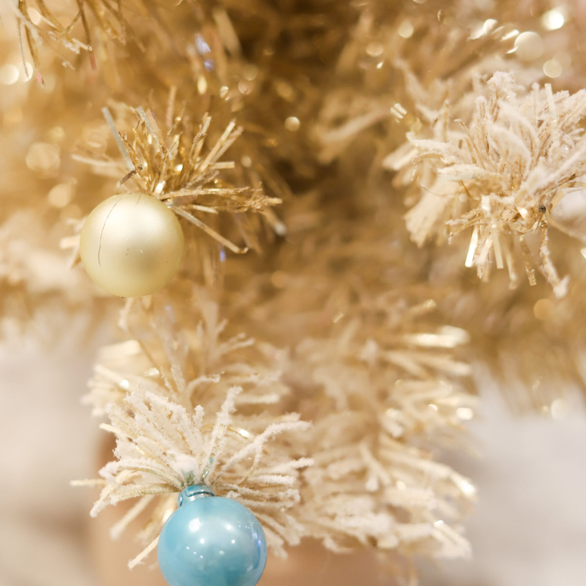 Gold tinsel Christmas tree with snowy flocking and colorful ornaments. A whimsical 24-inch holiday accent for mantels, tabletops, consoles, and festive displays.