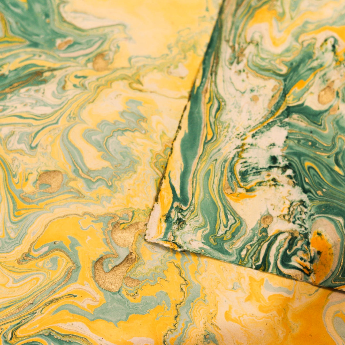 Marbled paper sheets with a swirling pattern of yellow, green, white, and beige, arranged overlapping.