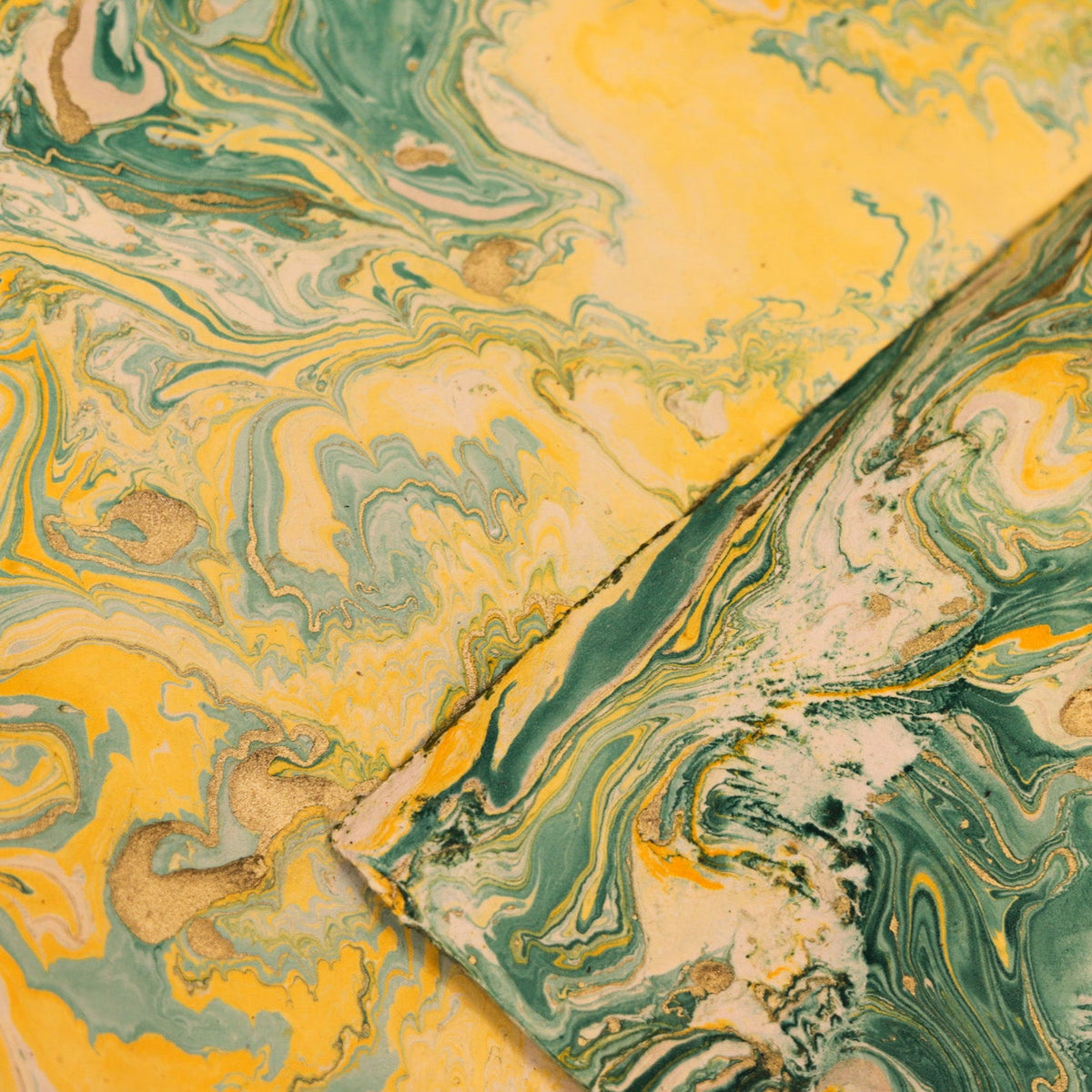 A close-up of a folded sheet of marbled paper or fabric with an abstract swirl pattern in yellow, green, cream, and small gold flecks.