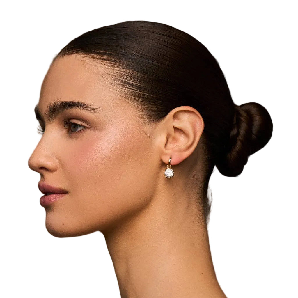 Woman with a stylish hair bun wearing earrings against a neutral background