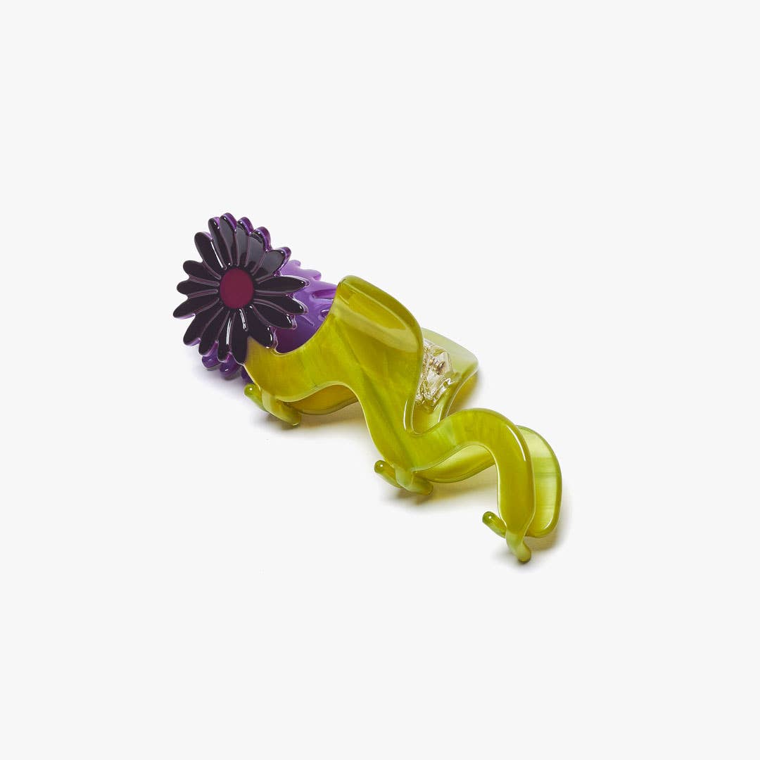 The Wavy Daisy Hair Claw features a sculptural chartreuse design with a dimensional purple flower, crafted from cellulose acetate for a playful statement.