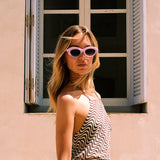 Woman wearing pink sunglasses and a patterned outfit in front of a window.