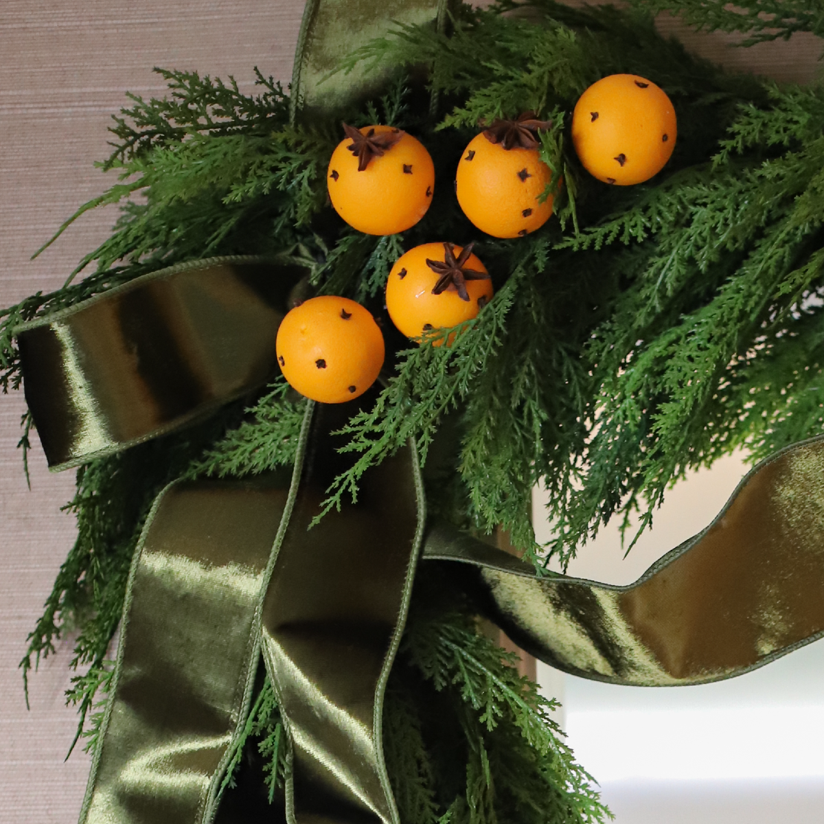 Clementine and Clove Pomander Spray arranged in evergreen greenery with olive velvet ribbon