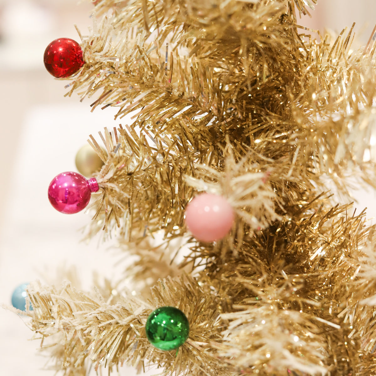 Gold tinsel Christmas tree with snowy flocking and colorful ornaments. A whimsical 24-inch holiday accent for mantels, tabletops, consoles, and festive displays.