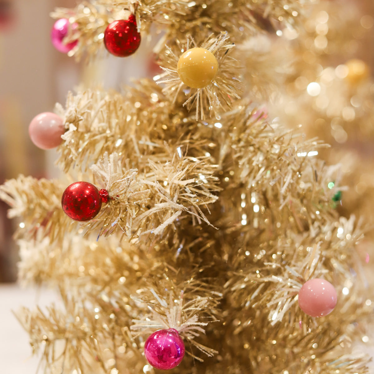 Gold tinsel Christmas tree with snowy flocking and colorful ornaments. A whimsical 24-inch holiday accent for mantels, tabletops, consoles, and festive displays.