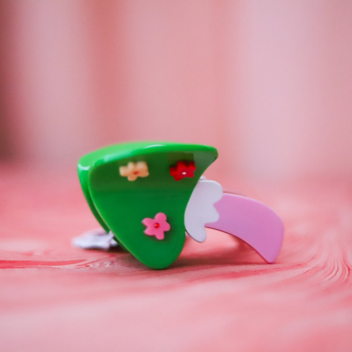 The Flower Mushroom Hair Claw features a glossy green cap, colorful floral details and a pink stem, handmade from playful cellulose acetate.