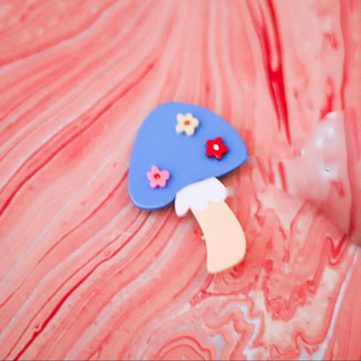 The Blue Flower Mushroom Hair Clip features a bright blue cap, colorful floral details and a yellow stem, handmade from cellulose acetate.