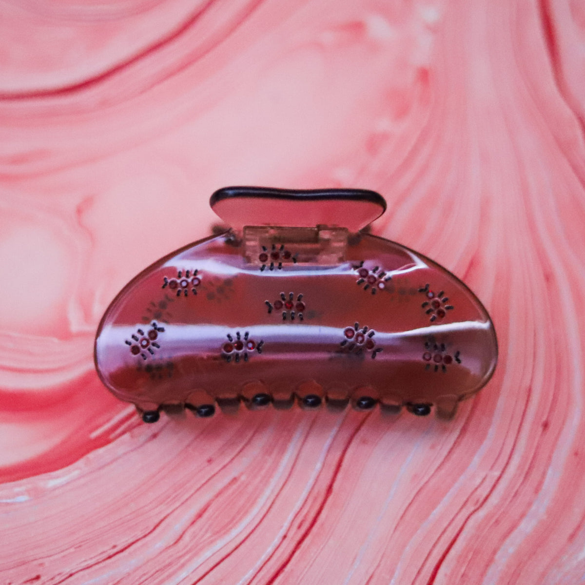 The Fire Ant Hair Claw features dark red rhinestone ants on a translucent blush-purple cellulose acetate claw for a playful, unexpected statement.