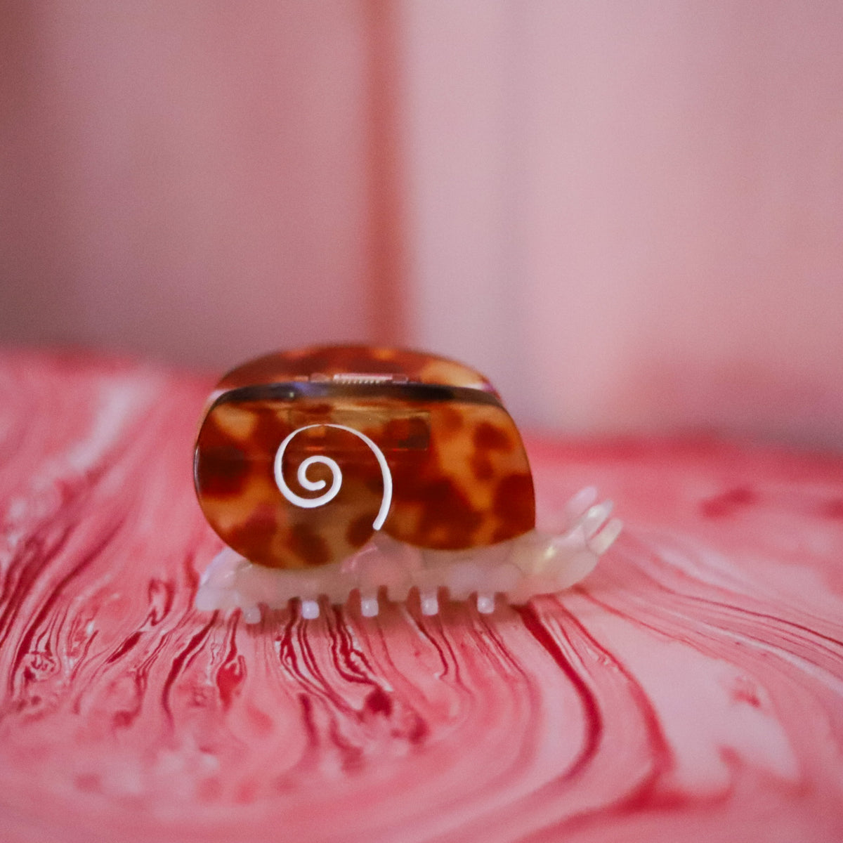 The Sea Snail Hair Claw features a pearlescent body and amber tortoise shell, crafted from individually cut cellulose acetate for a playful statement.