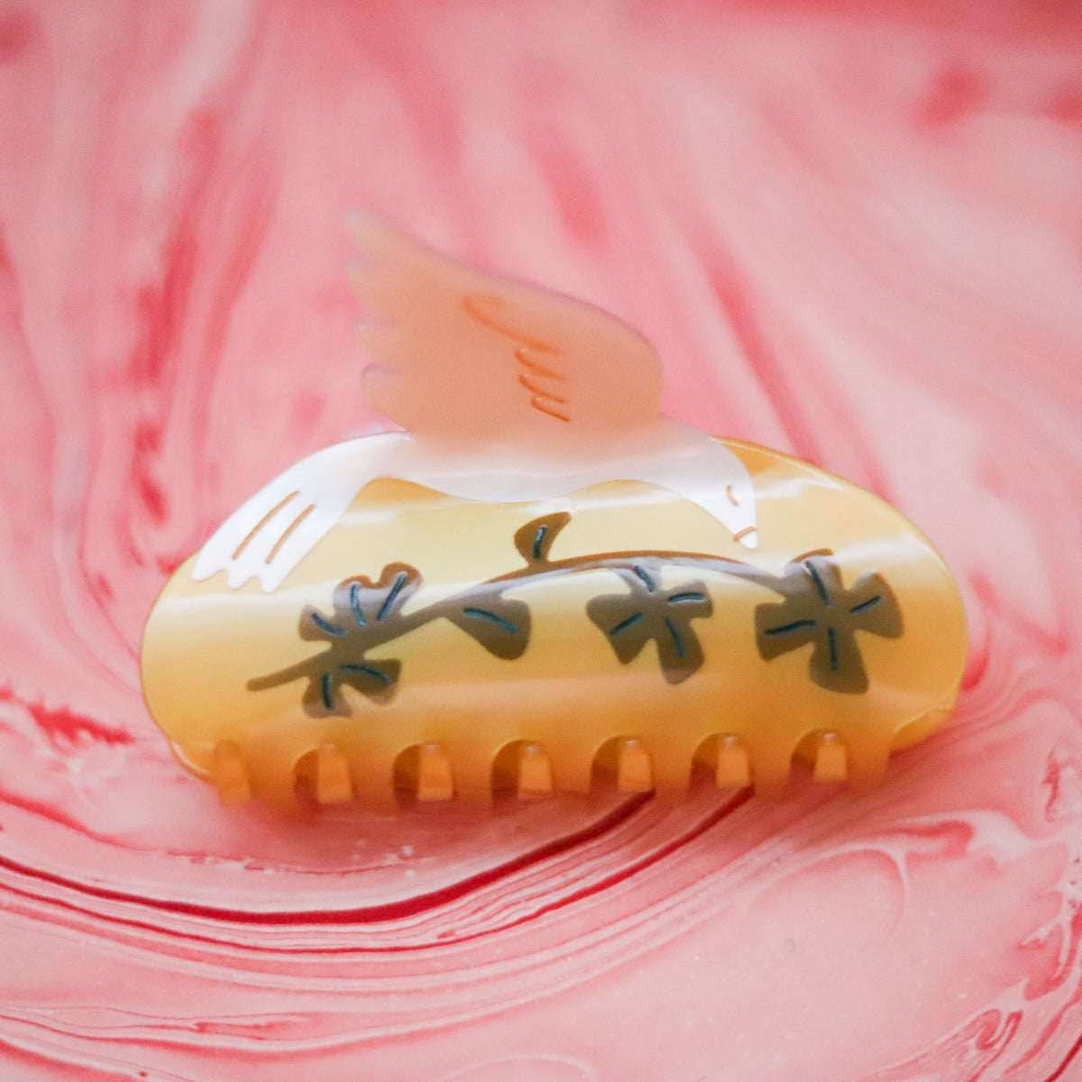 The Lucky Dove Hair Claw features a graceful bird design with golden, blush and botanical details, crafted from individually cut cellulose acetate.