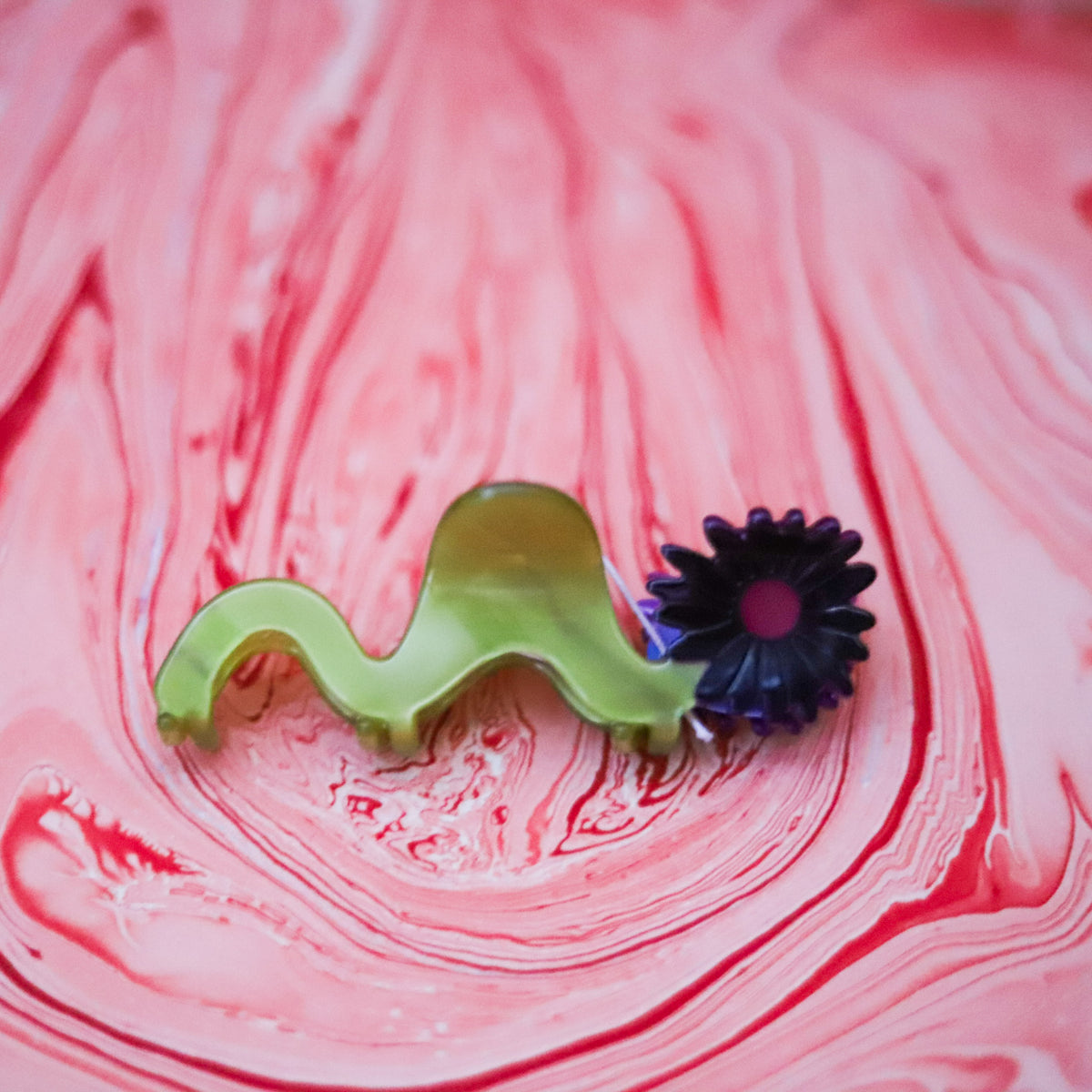 The Wavy Daisy Hair Claw features a sculptural chartreuse design with a dimensional purple flower, crafted from cellulose acetate for a playful statement.