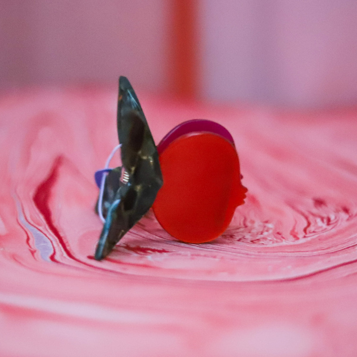 The Pomegranate Hair Claw features a glossy red fruit with deep green leaves and a whimsical butterfly-style handle for a playful botanical touch.