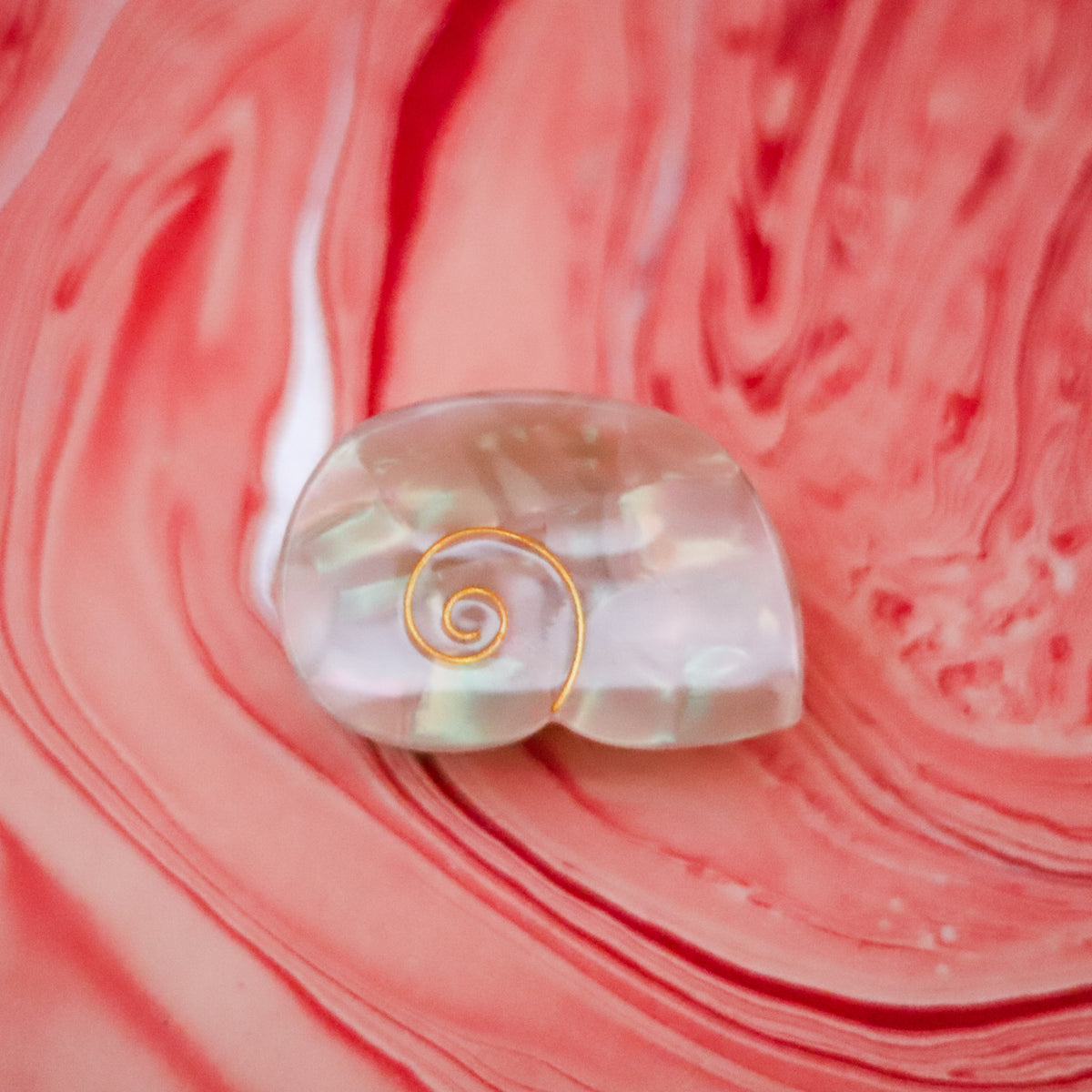 The Siren Hair Claw features a shimmering shell-inspired design with a pearlescent finish and delicate gold spiral detail, crafted from cellulose acetate.