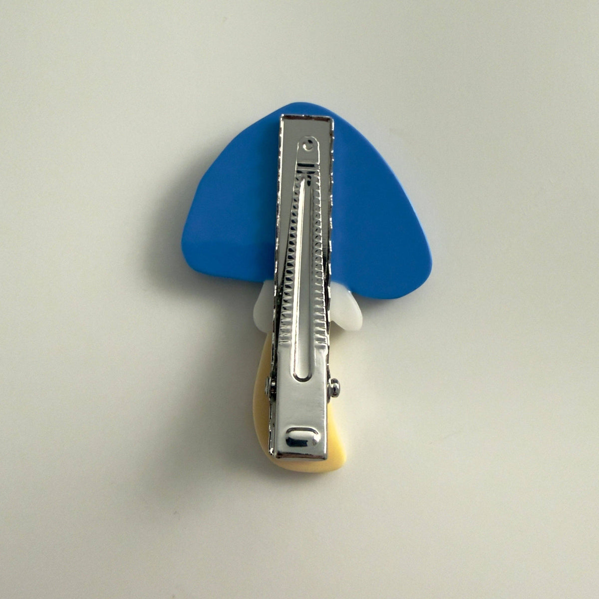 The Blue Flower Mushroom Hair Clip features a bright blue cap, colorful floral details and a yellow stem, handmade from cellulose acetate.