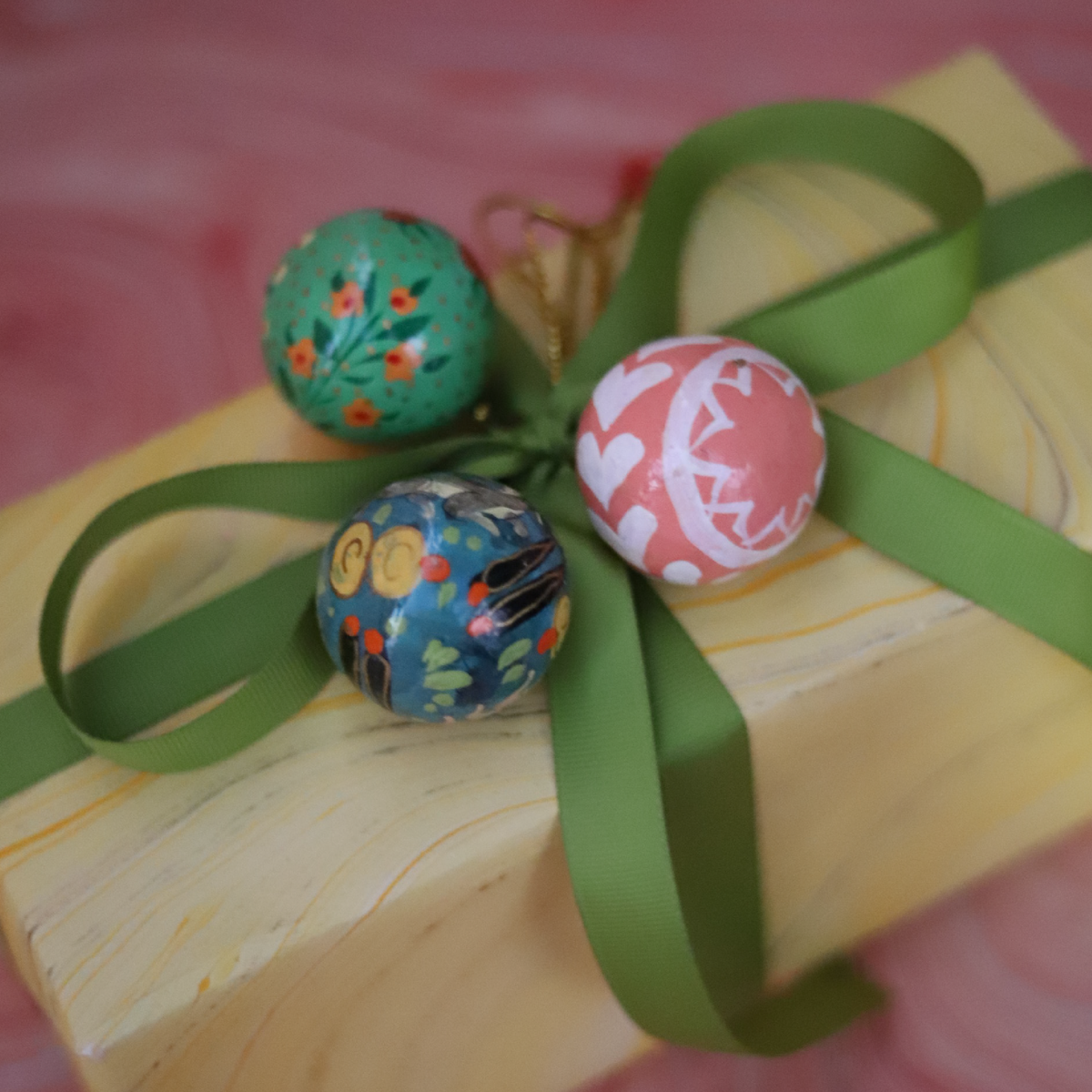 Red and ivory striped hand-painted paper mache gift bauble tied to a wrapped Christmas present with blue velvet ribbon