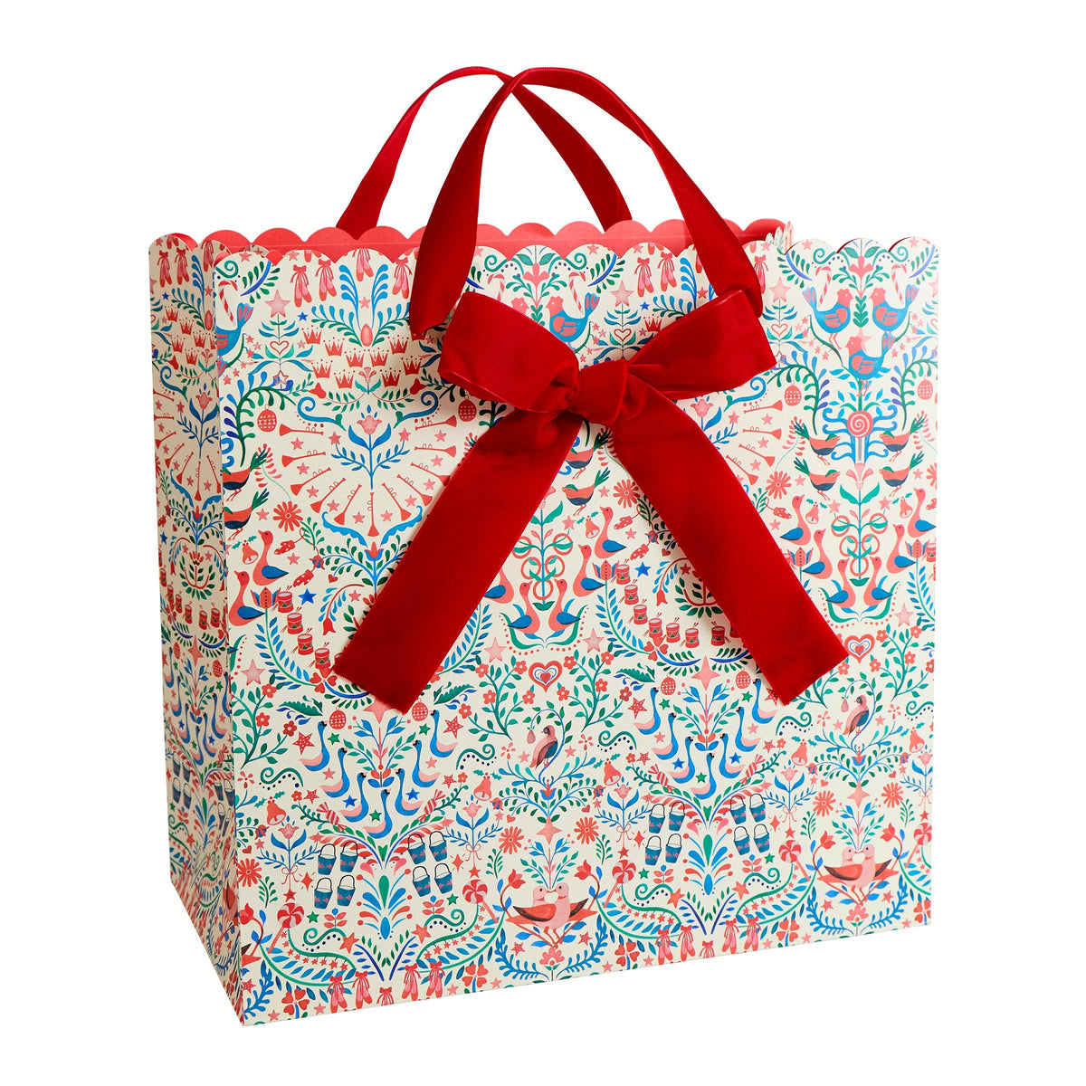 A decorative gift bag with a scalloped edge, featuring a colorful floral and bird pattern in blue, red, and green on a white background, complete with a large red ribbon bow and handles.